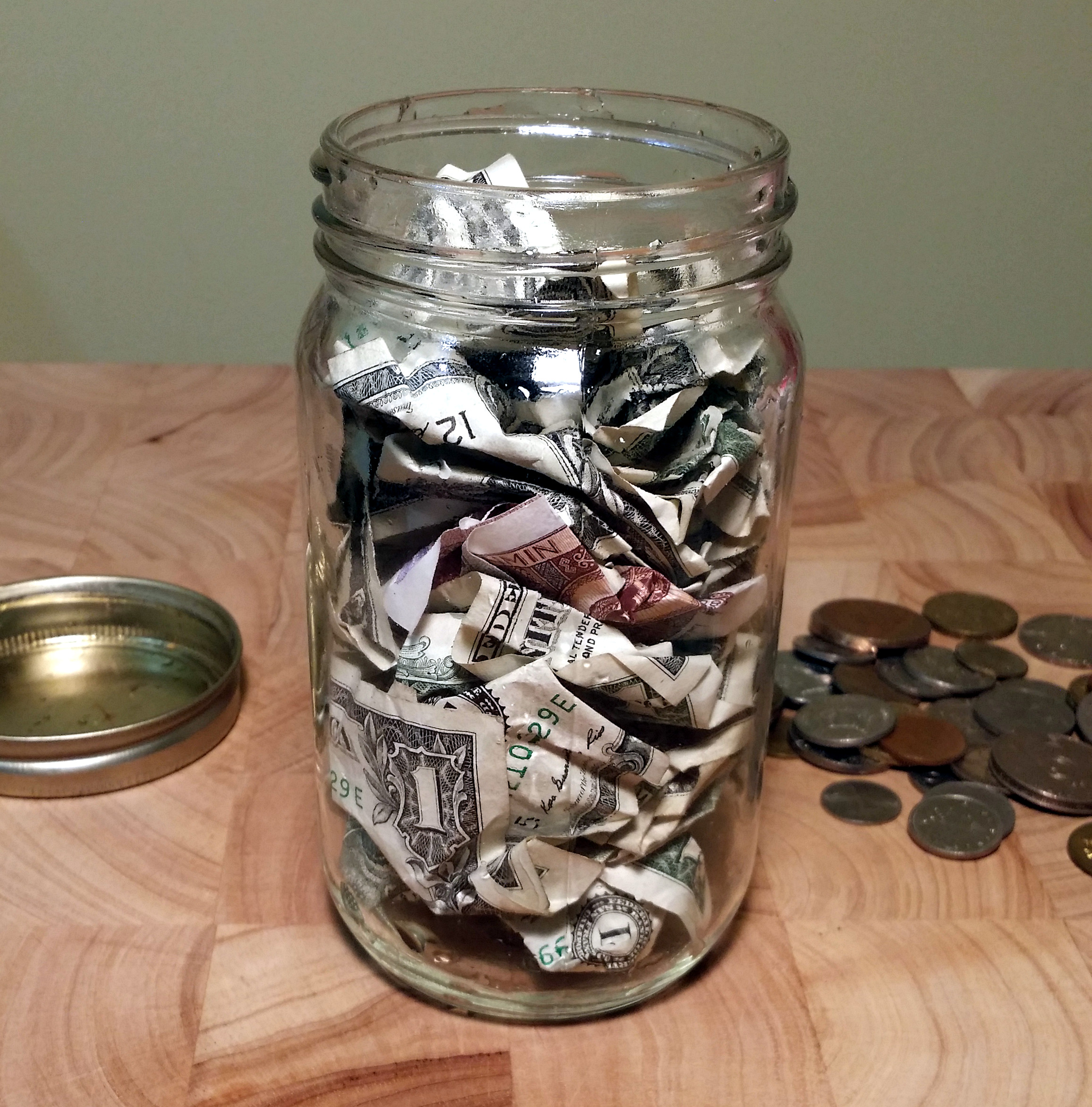 a jar stuffed with money and a pile of coins sit on a wooden background