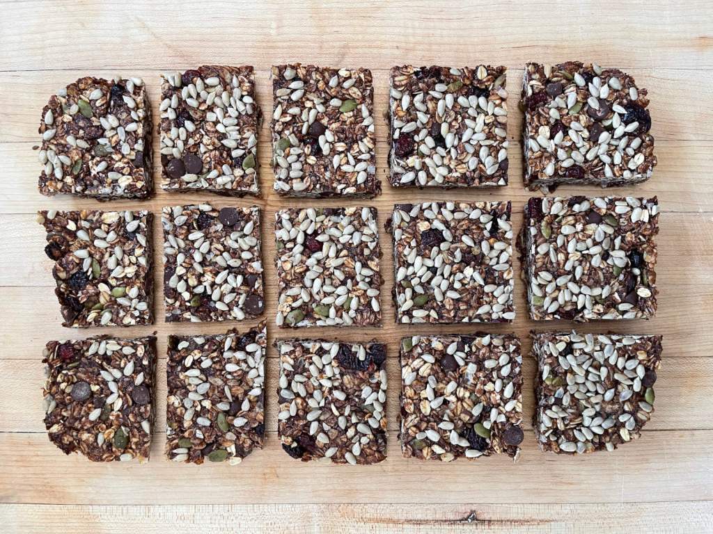 15 square chocolate granola bars sit on a blond wooden cutting board