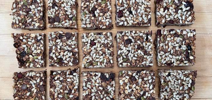 15 square chocolate granola bars sit on a blond wooden cutting board