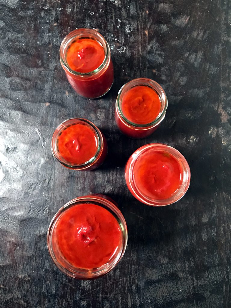five glass jars filled with tomato paste slow cooked in the oven