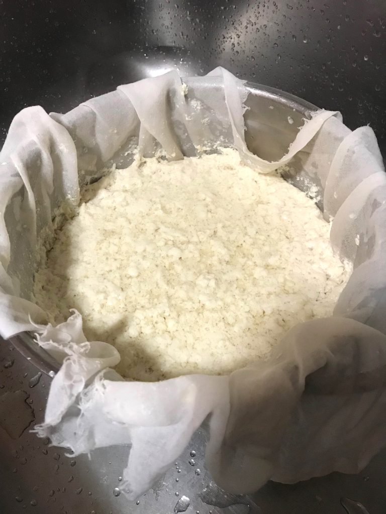 straining tofu curds in the kitchen sink for homemade tofu