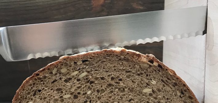 loaf of sourdough bread being sliced with a serrated knife