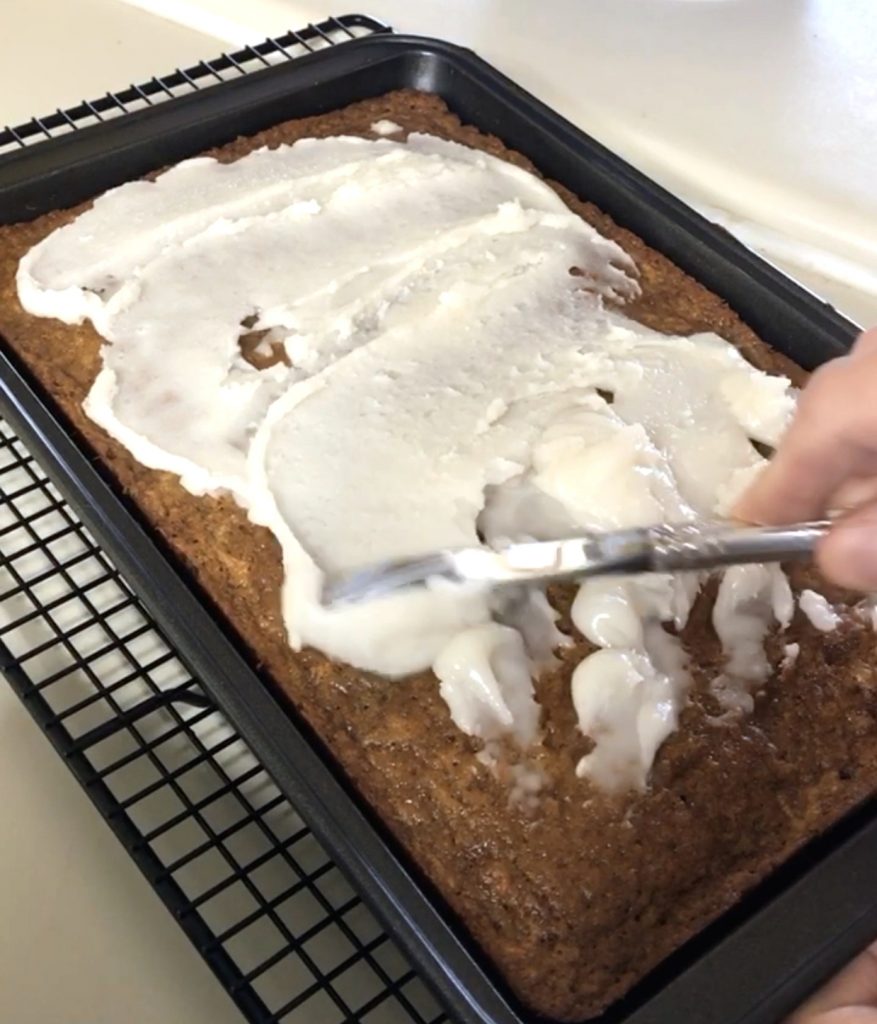 frosting a sourdough carrot cake in the pan with coconut buttercream frosting