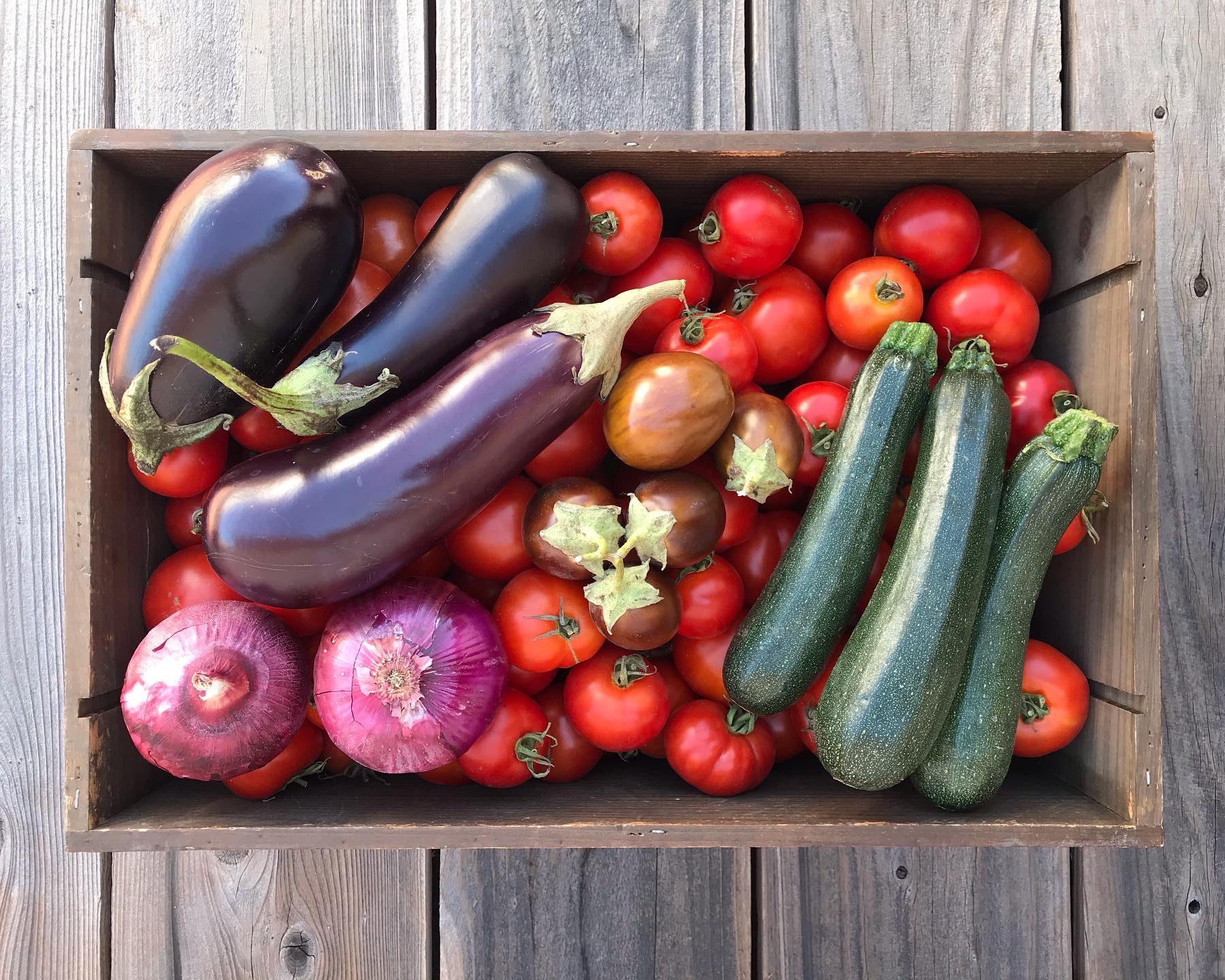 wooden crate filled with seasonal produce of tomatoes, eggplant, red onions and zucchini