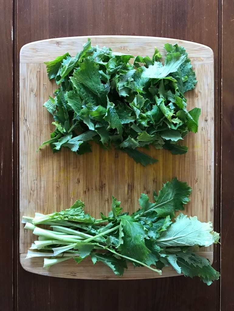 Leafy greens cut from the tops of turnips sit on a wooden cutting board