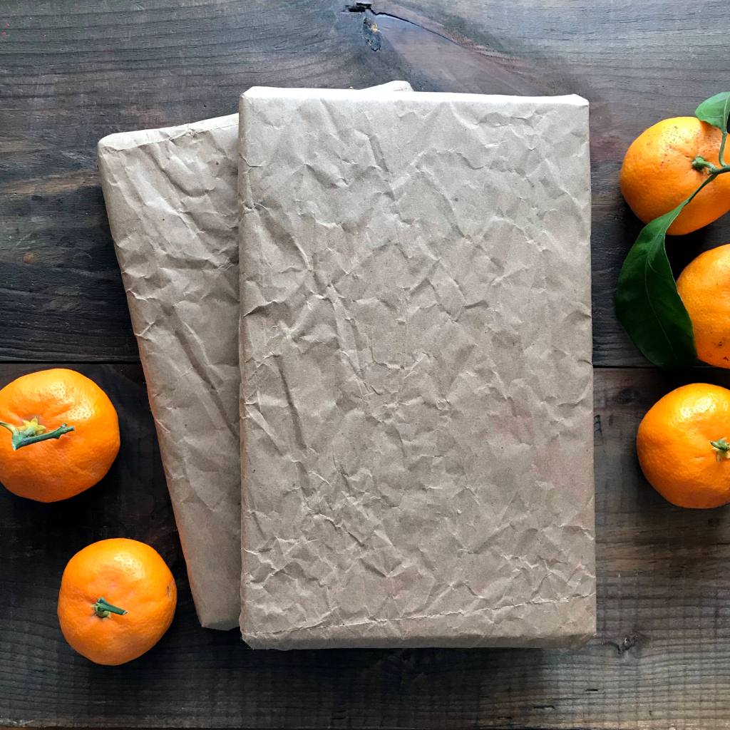 Holiday gifts wrapped in brown paper sit on a wooden background. Clementine oranges are on the left and right of the gifts.