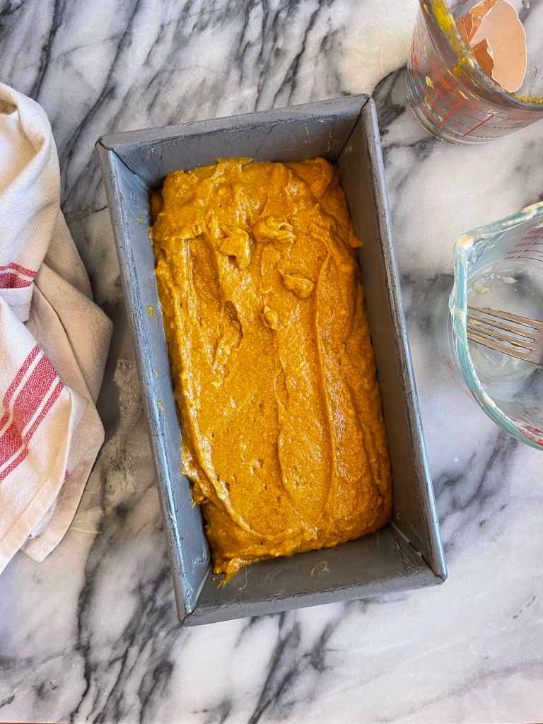 Sourdough pumpkin quick bread batter in a metal loaf pan sitting on a grey and white marble background