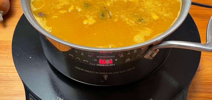 A pot of soup cooking on a portable induction cooktop that is sitting on a wooden table