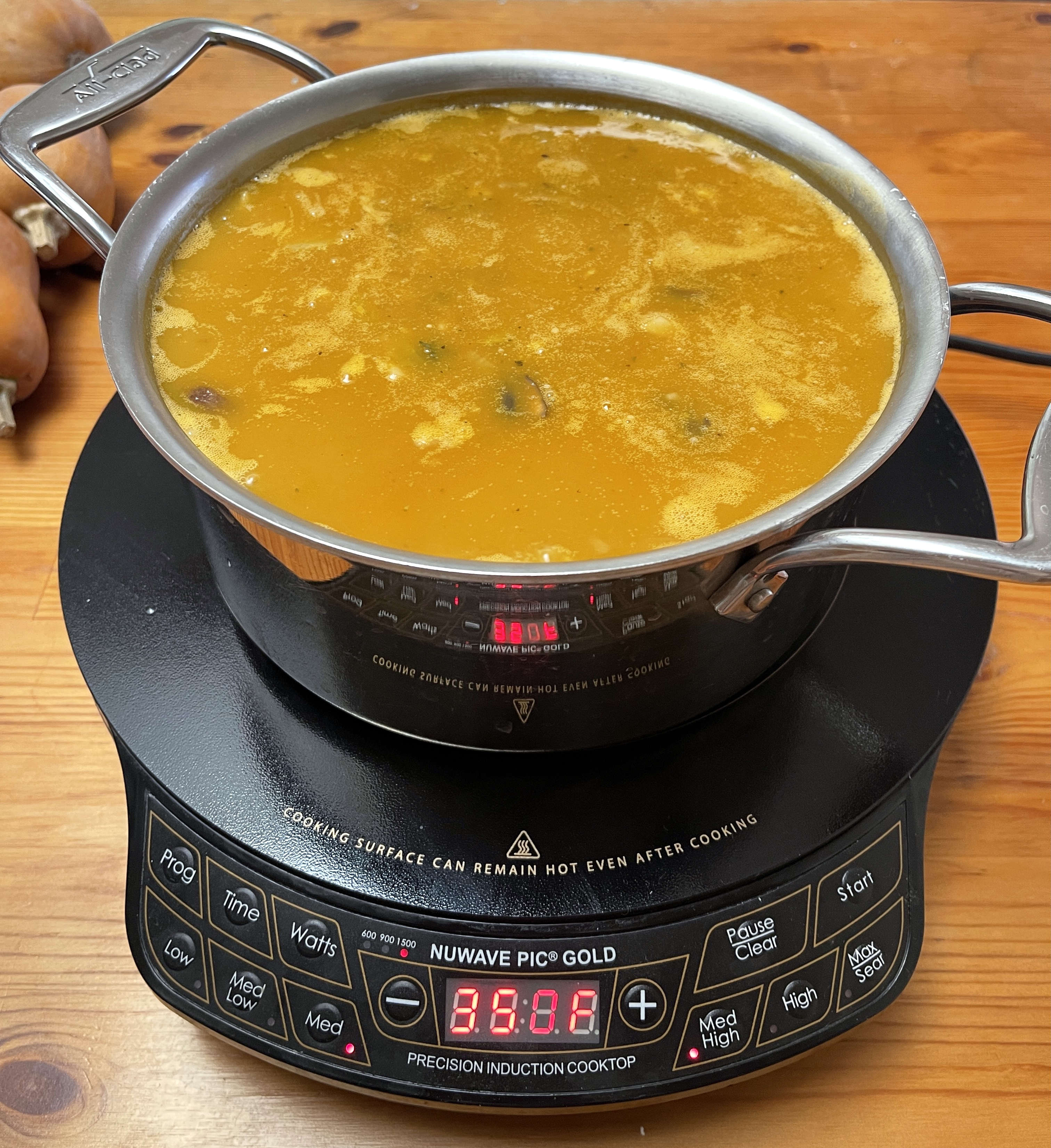 A pot of soup cooking on a portable induction cooktop that is sitting on a wooden table