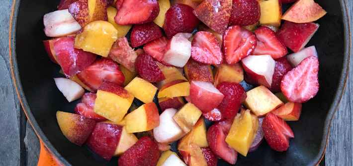 A cast iron pan with an orange handle is filled with fresh fruit to bake a crumble and reduce wasted food