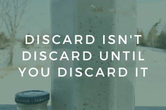 A very small jar next to a very large jars of sourdough starter is faded out with text appearing across the image, saying "Discard isn't discard until you discard it"