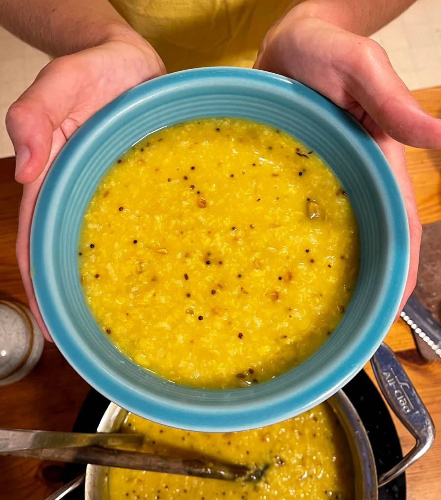 A turquoise bowl is filled with cooked khichdi. Two hands hold the bowl up.