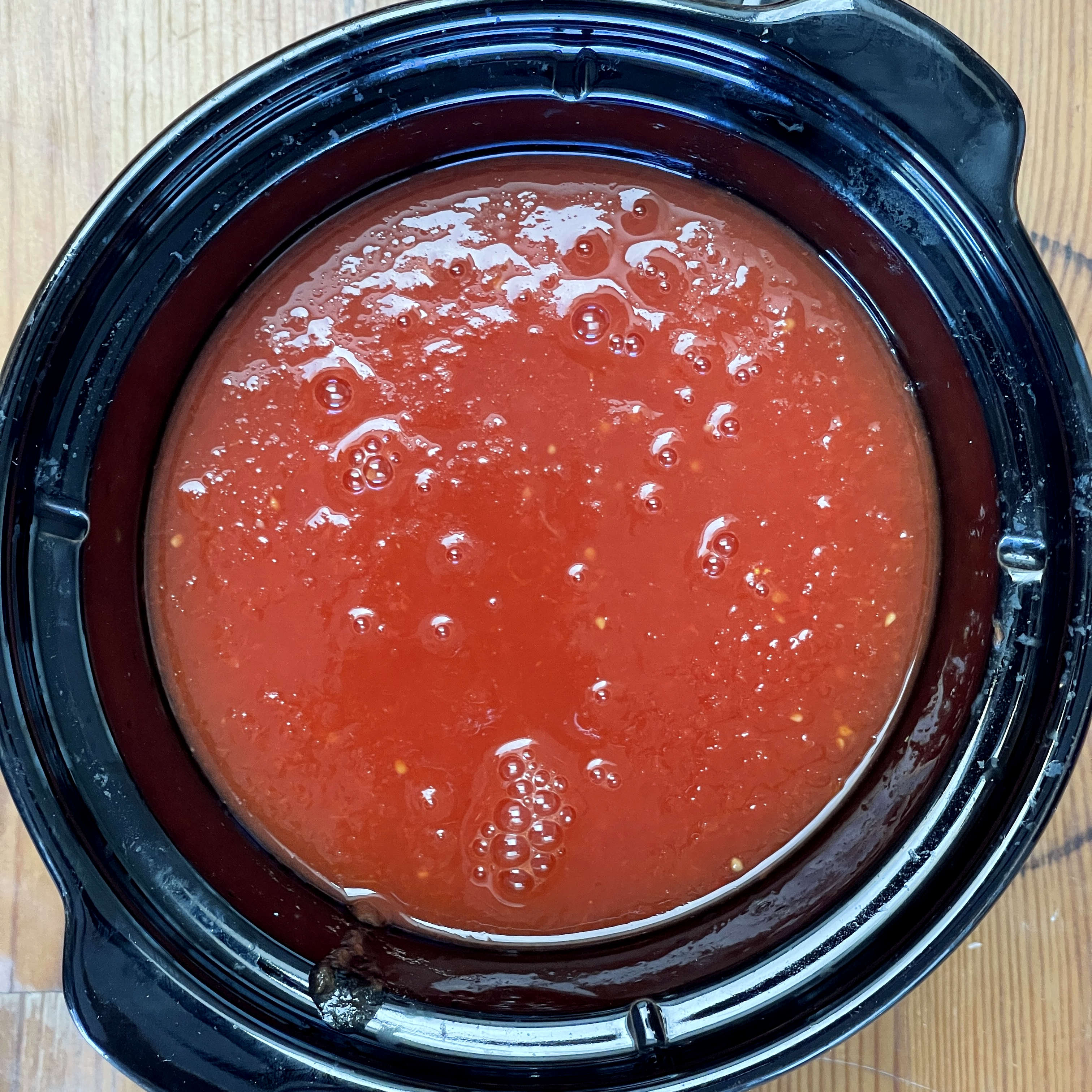 The black crock of a slow cooker is filled with puréed tomatoes to cook down into tomato sauce