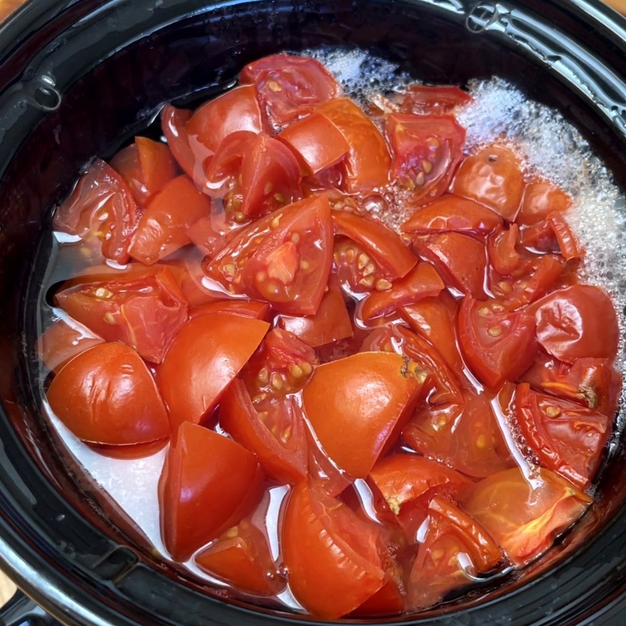Chopped fresh tomatoes in a small black slow cooker crock have cooked down and softened