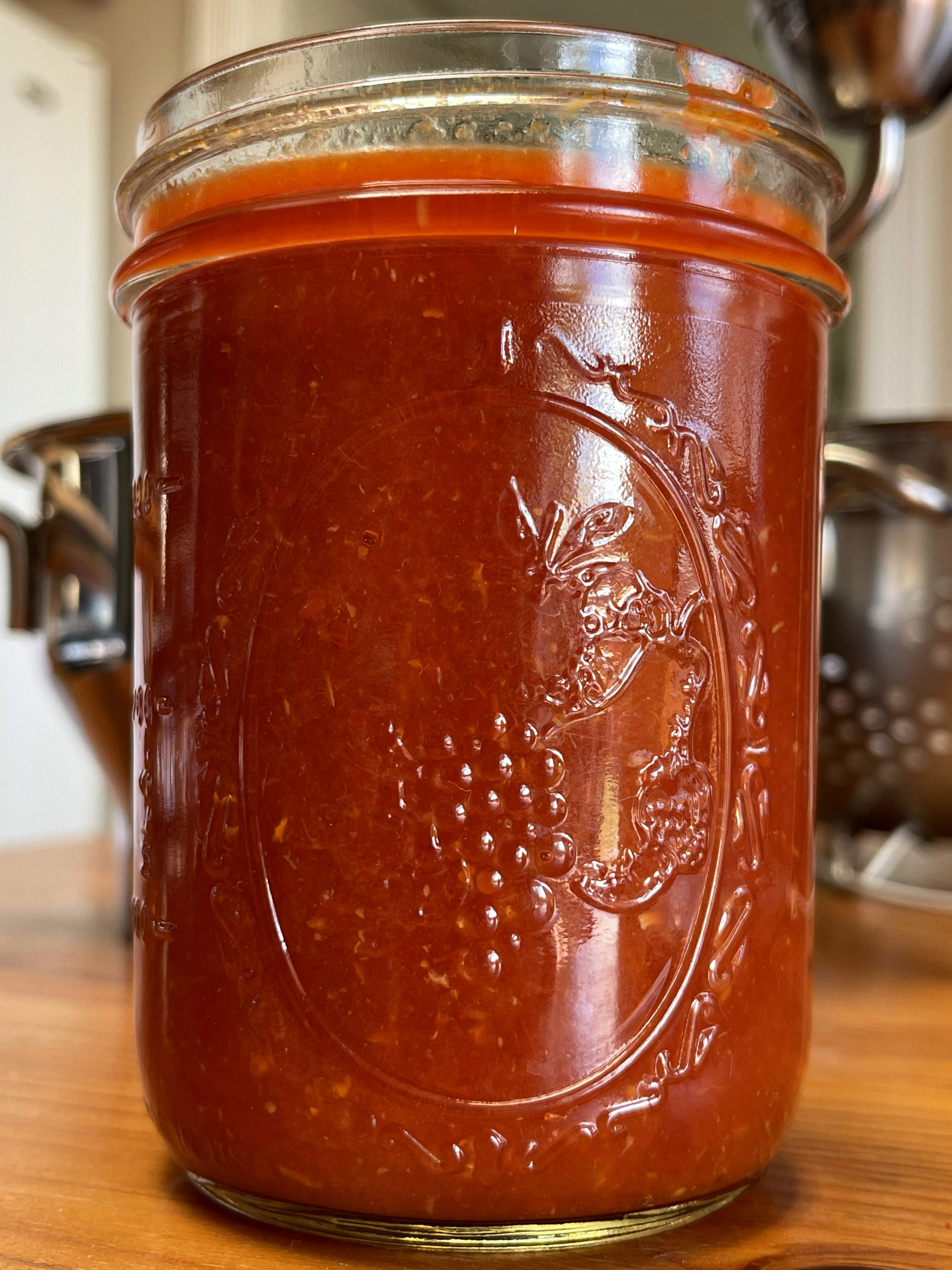 A mason jar is filled with homemade tomato purée. The jars sits on a wooden table.