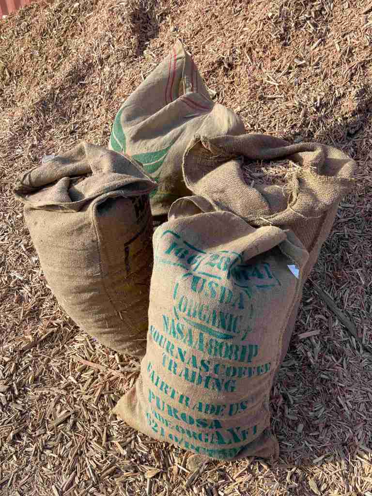 Burlap sacks filled with wood chips sit in front of a giant pile of wood chips