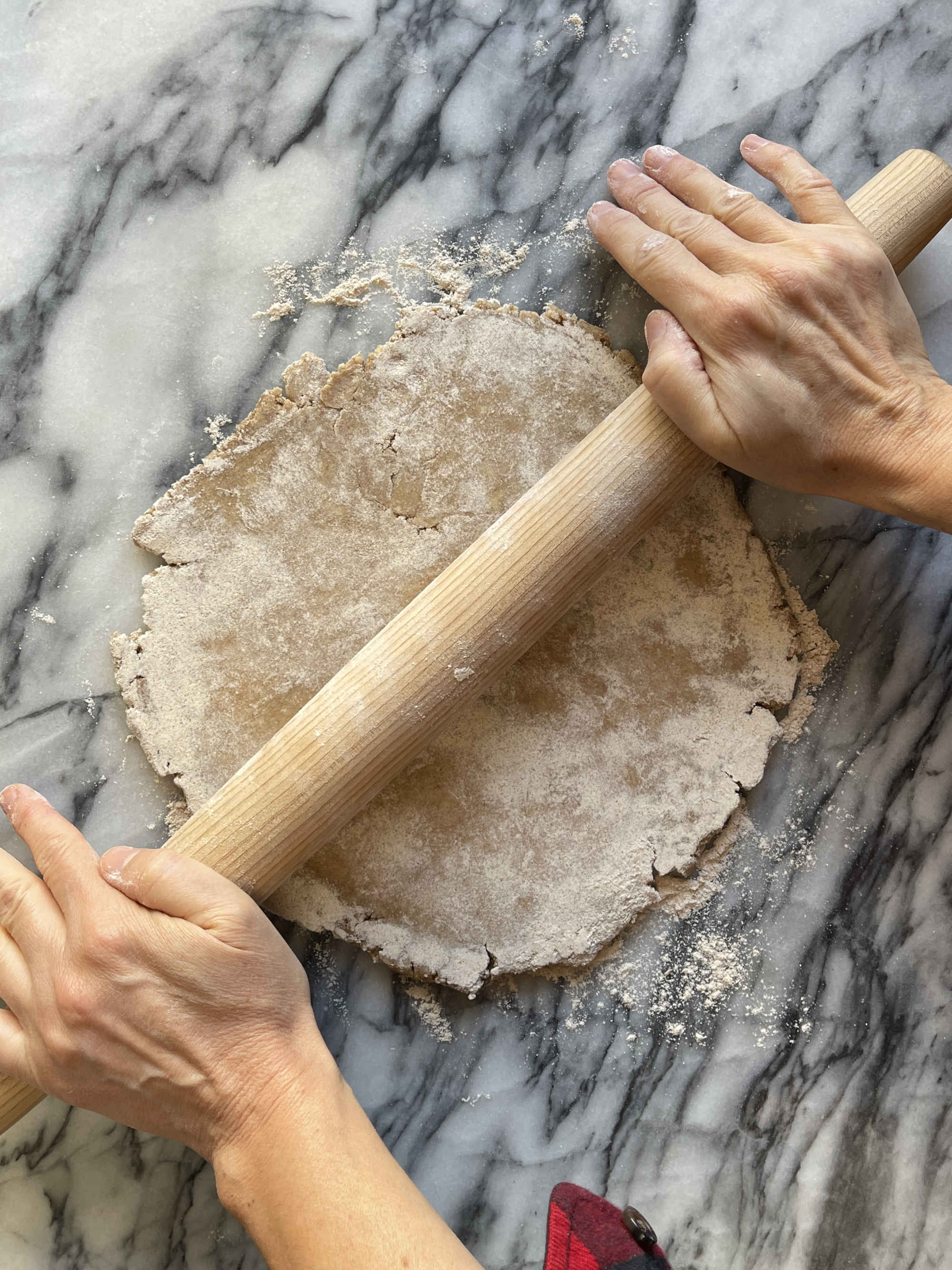 Hands roll out whole wheat pastry with a tapered rolling pin on grey and white marble