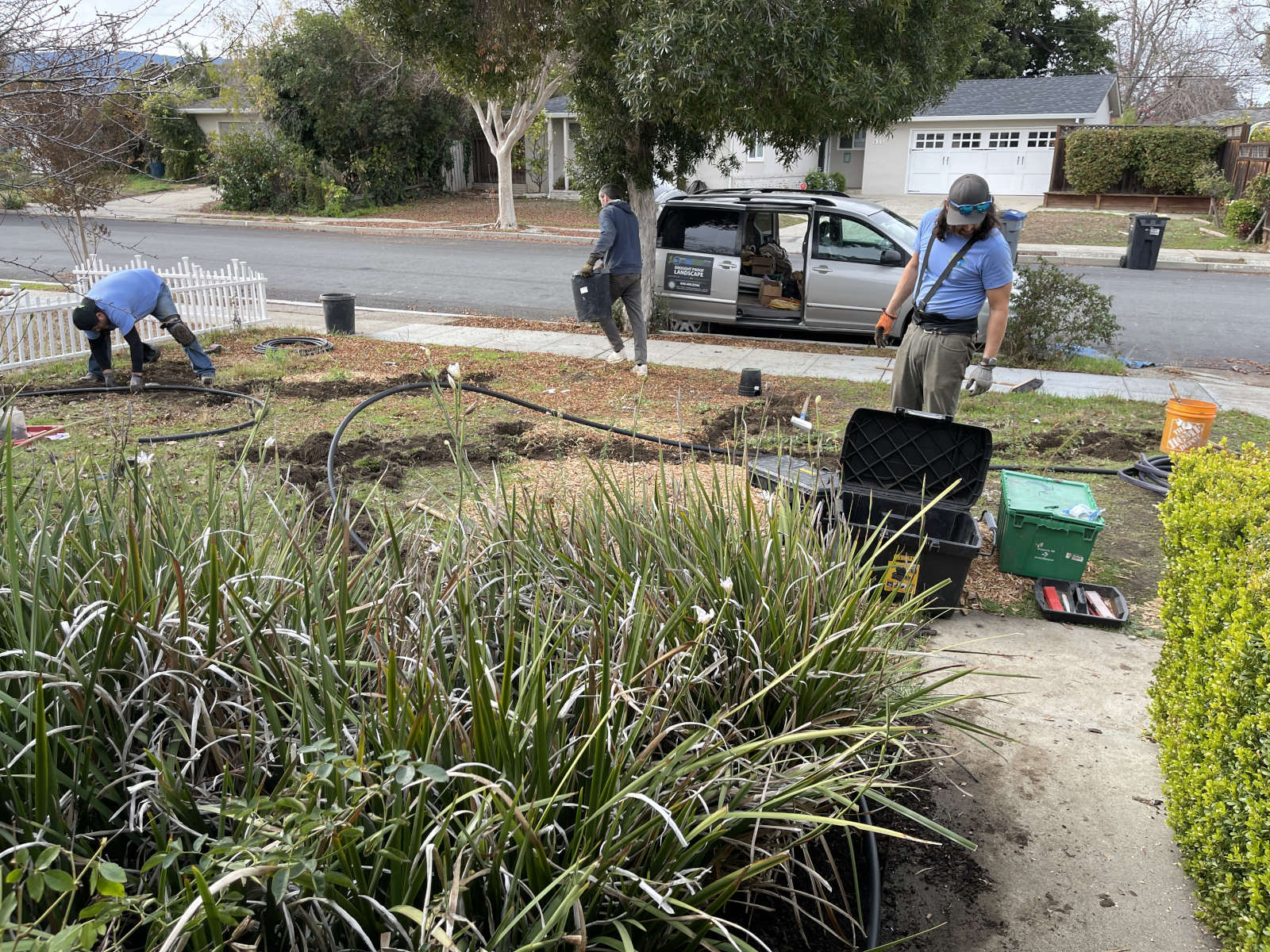 Three men wearing blue shirts are working on a greywater system in a yard
