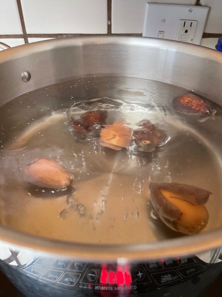 Six avocado pits bob around in a pot of simmering water to make natural pink avocado pit dye