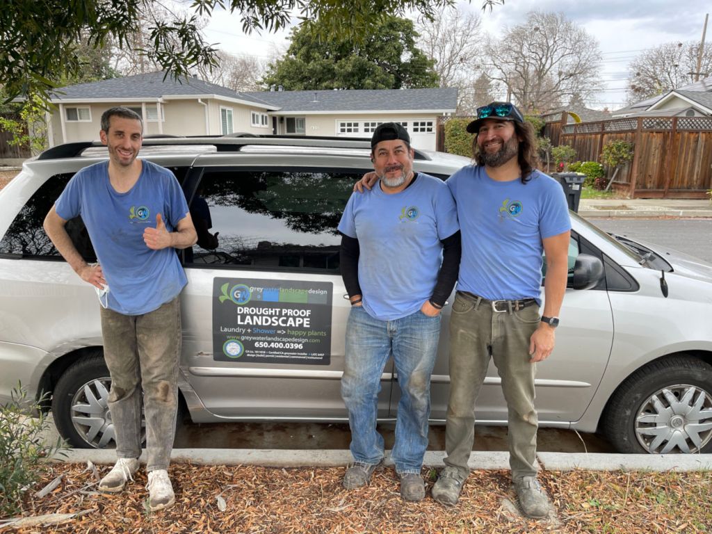 Three men in blue shirts stand in front of their silver van