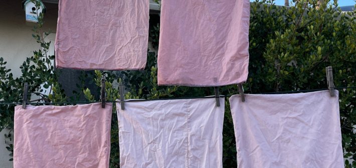 Five reusable cloth produce bags in varying shades of pink dry on a clothes line outside