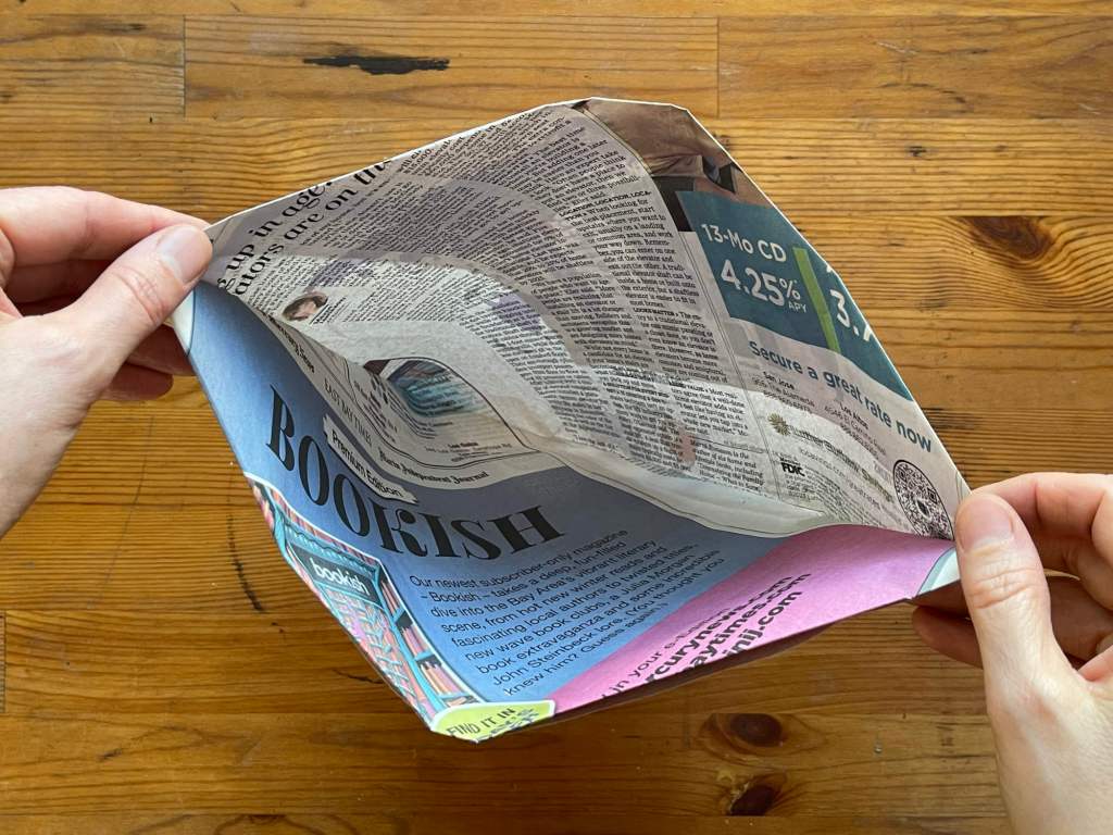 Hands hold open a compost bin liner made out of folded newspaper