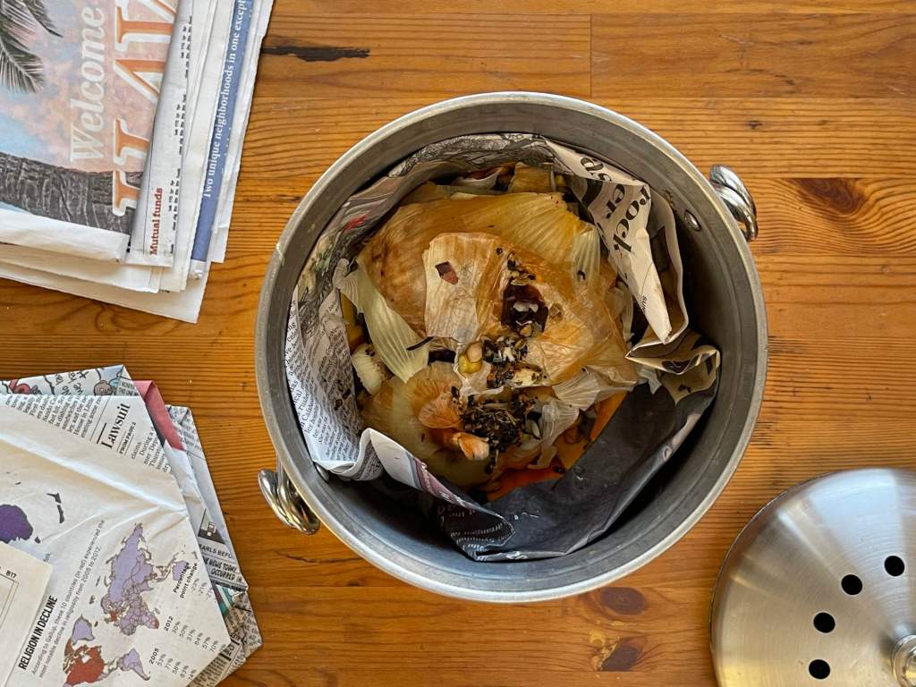 A compost bin is lined with a newspaper bin liner. The bag is filled with inedible food scraps.