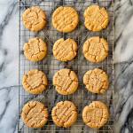 A dozen peanut butter cookies made with a sourdough discard flax egg cools in a cooling rack. The rack sits on a white and grey marble background.