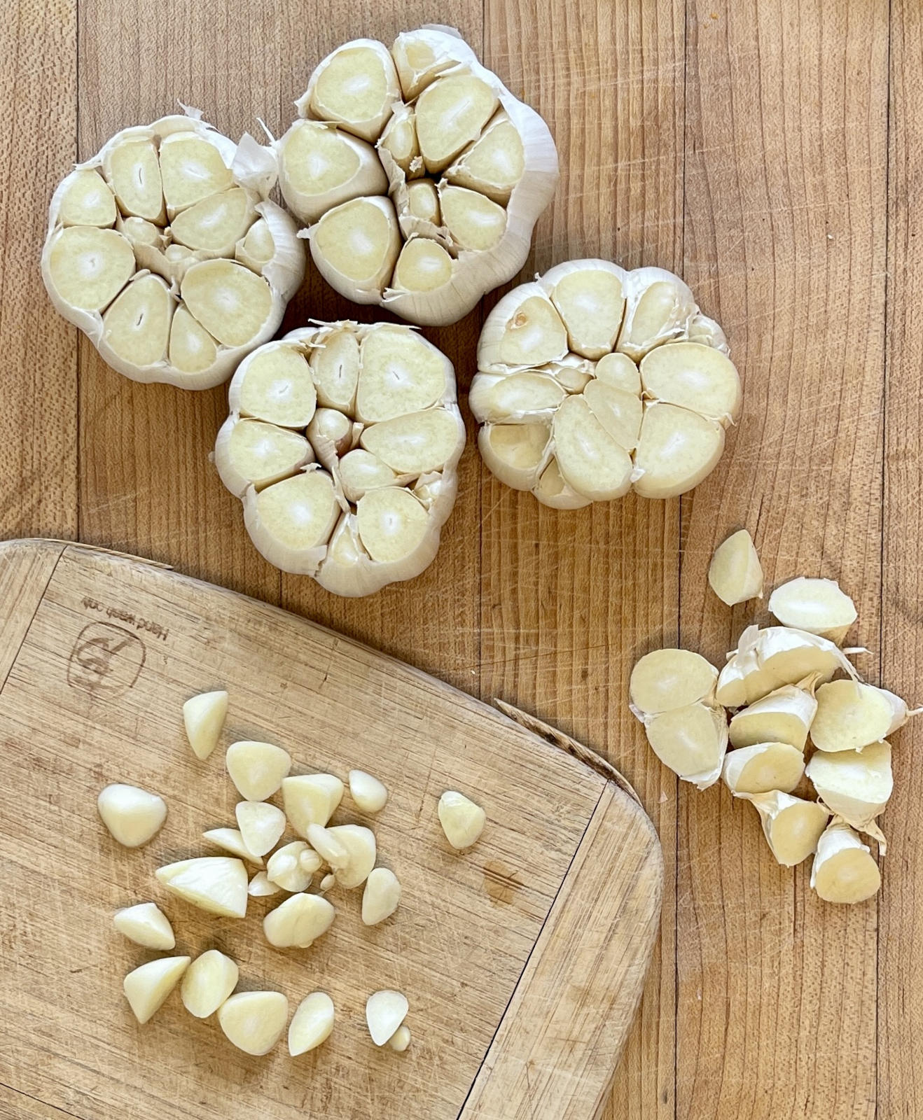 Four heads of garlic with the tops sliced off. The slices are sitting in two piles. Everything sits on light wooden cutting boards.