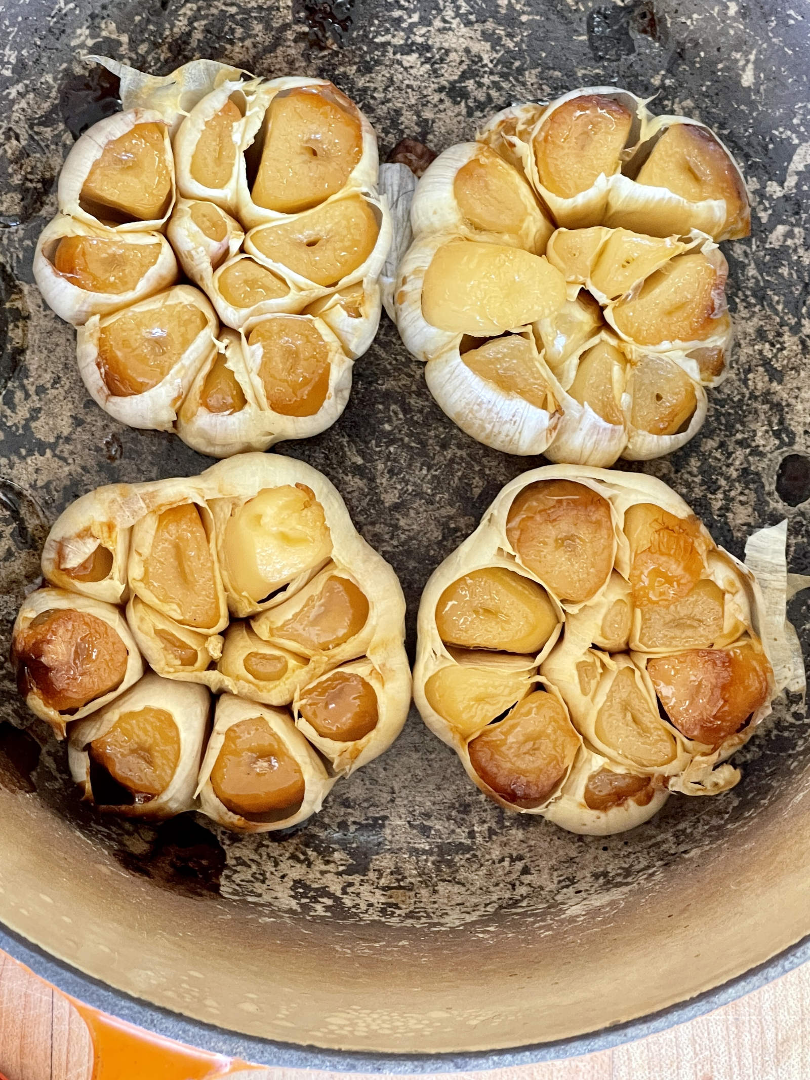 Four heads of roasted heads of garlic sit inside a Dutch oven.
