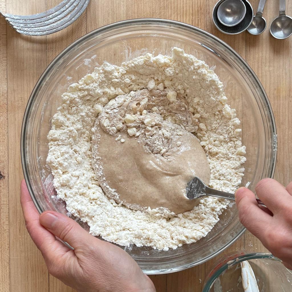 Hands mixing together sourdough biscuit ingredients in a bowl