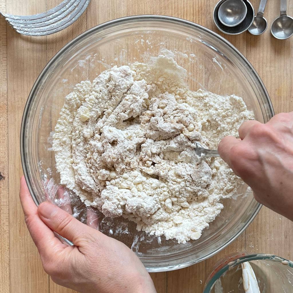 Hands mixing sourdough discard biscuit ingredients in a glass bowl
