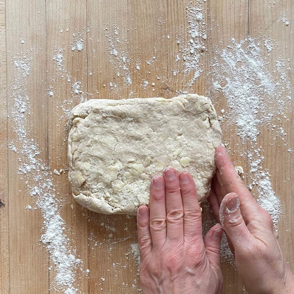 Hands form a rectangle of sourdough biscuit dough