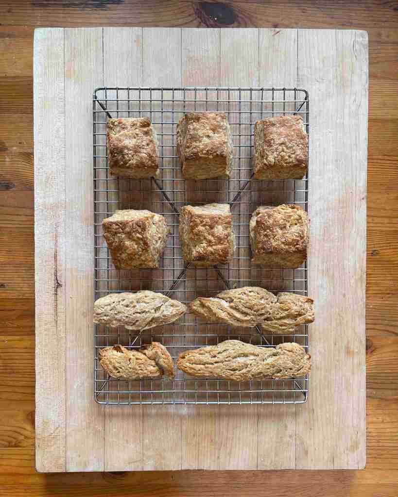 Baked sourdough biscuits cooling on a rack sitting on a light wooden board