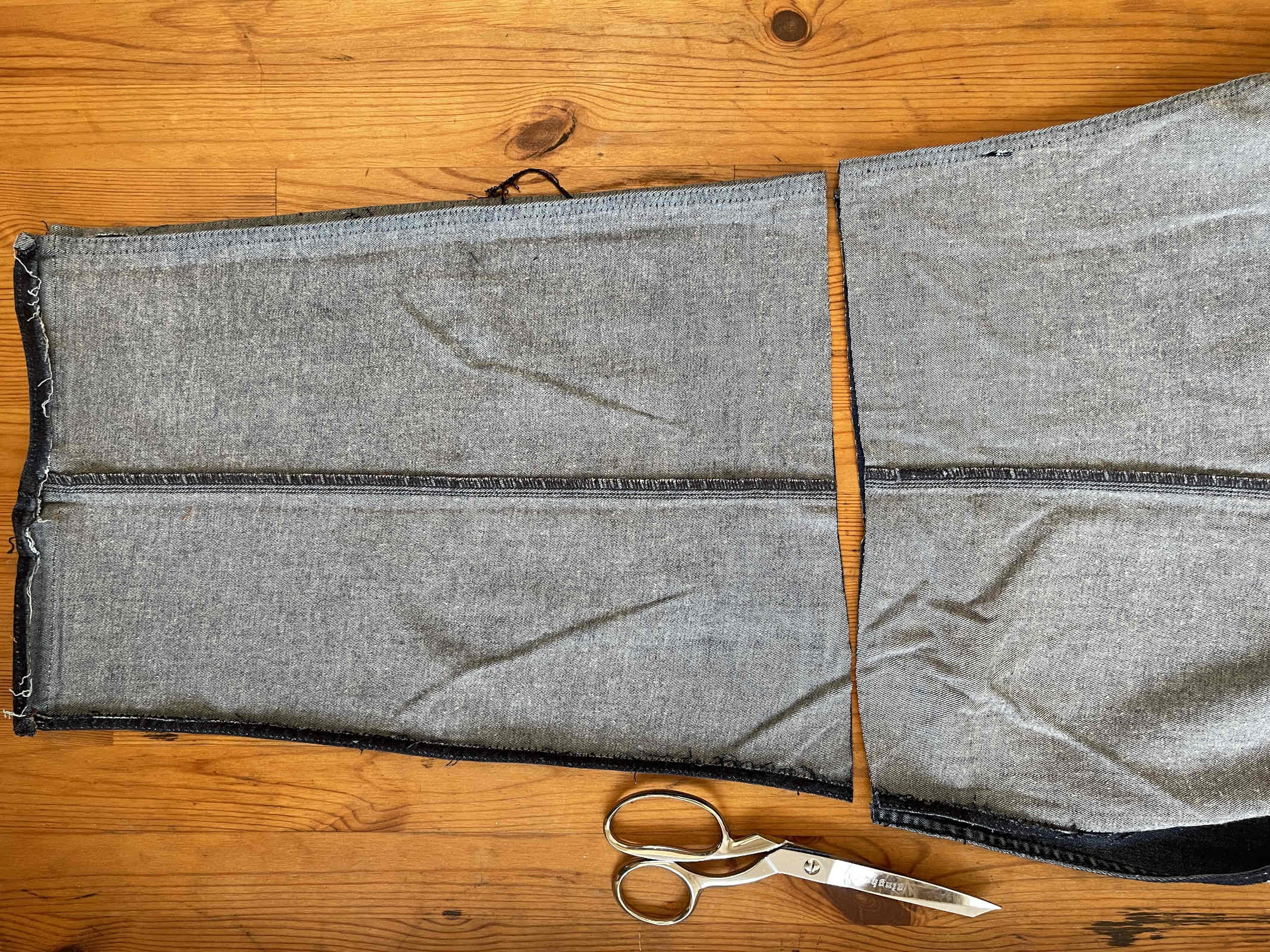 Cut jean legs sit on a wooden background with a pair of silver sewing shears