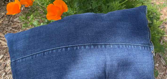 A denim garden kneeling pad outside. In the background are blooming orange California poppies.