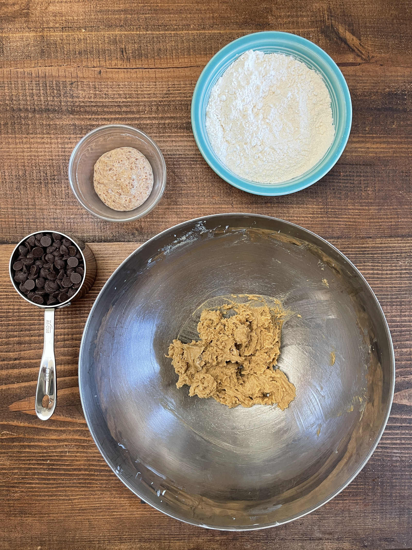 Chocolate chip cookie ingredients sit in bowls of various sizes sitting on a dark wooden background