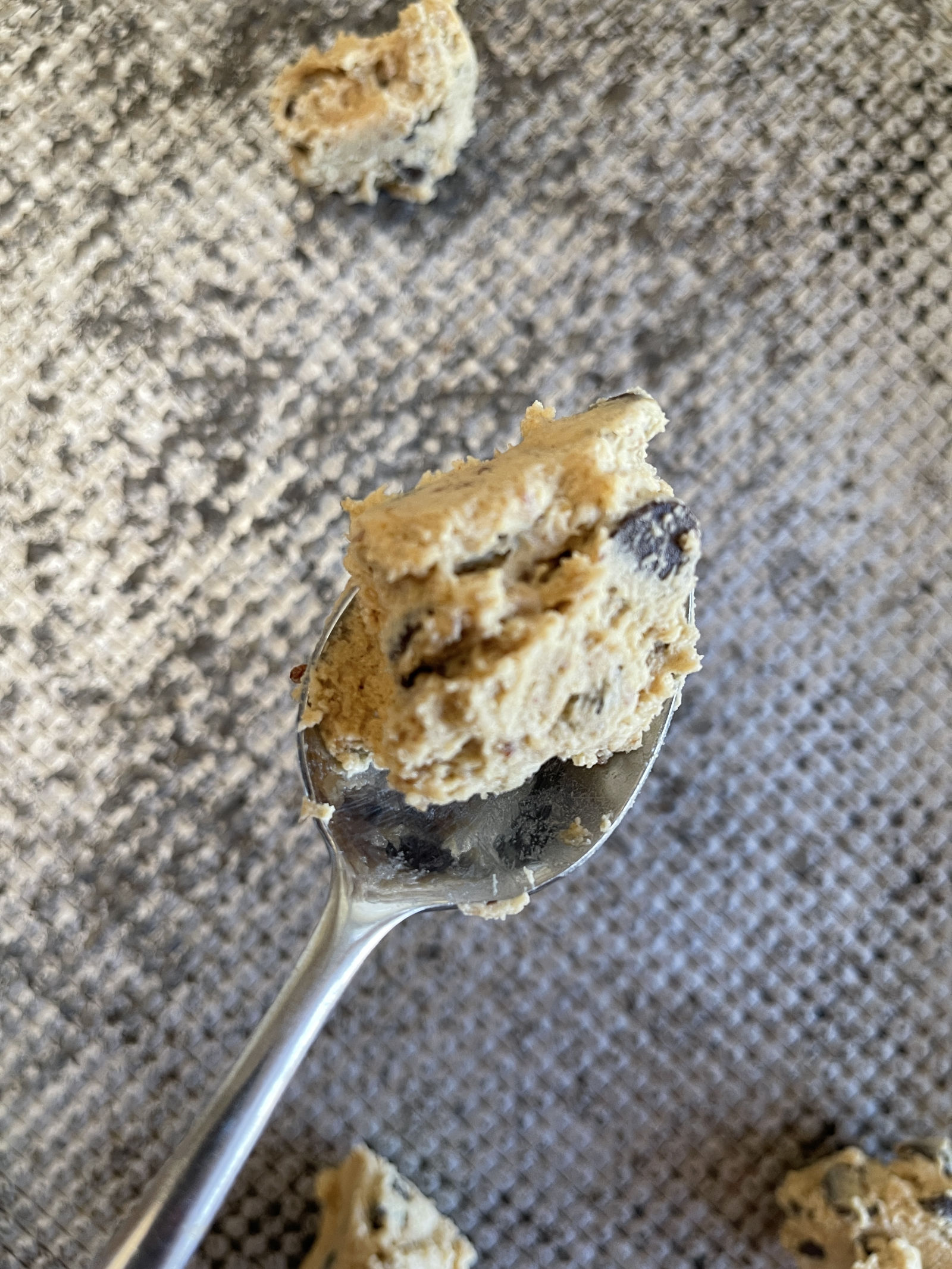 A spoonful of chocolate chip cookie dough with a sourdough discard flax egg. A cookie sheet in the background has spoonfuls of cookie dough sitting on it.
