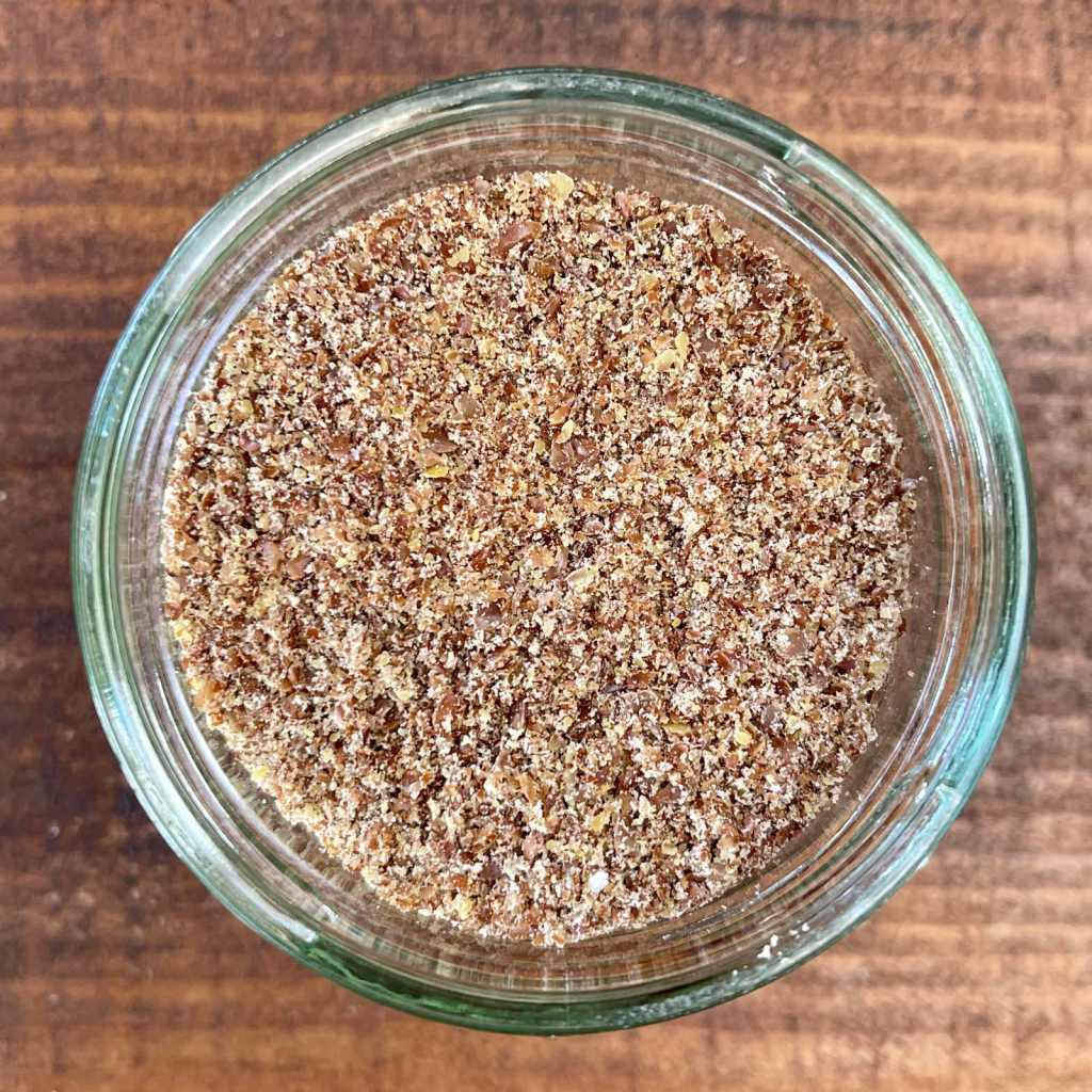 a closeup of a small jar of ground brown flaxseed, or flaxseed meal