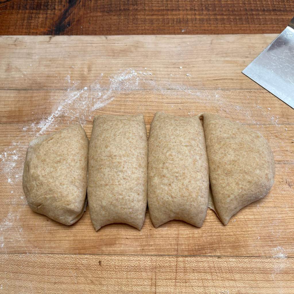 Tortilla dough cut into four pieces sits on a wooden cutting board