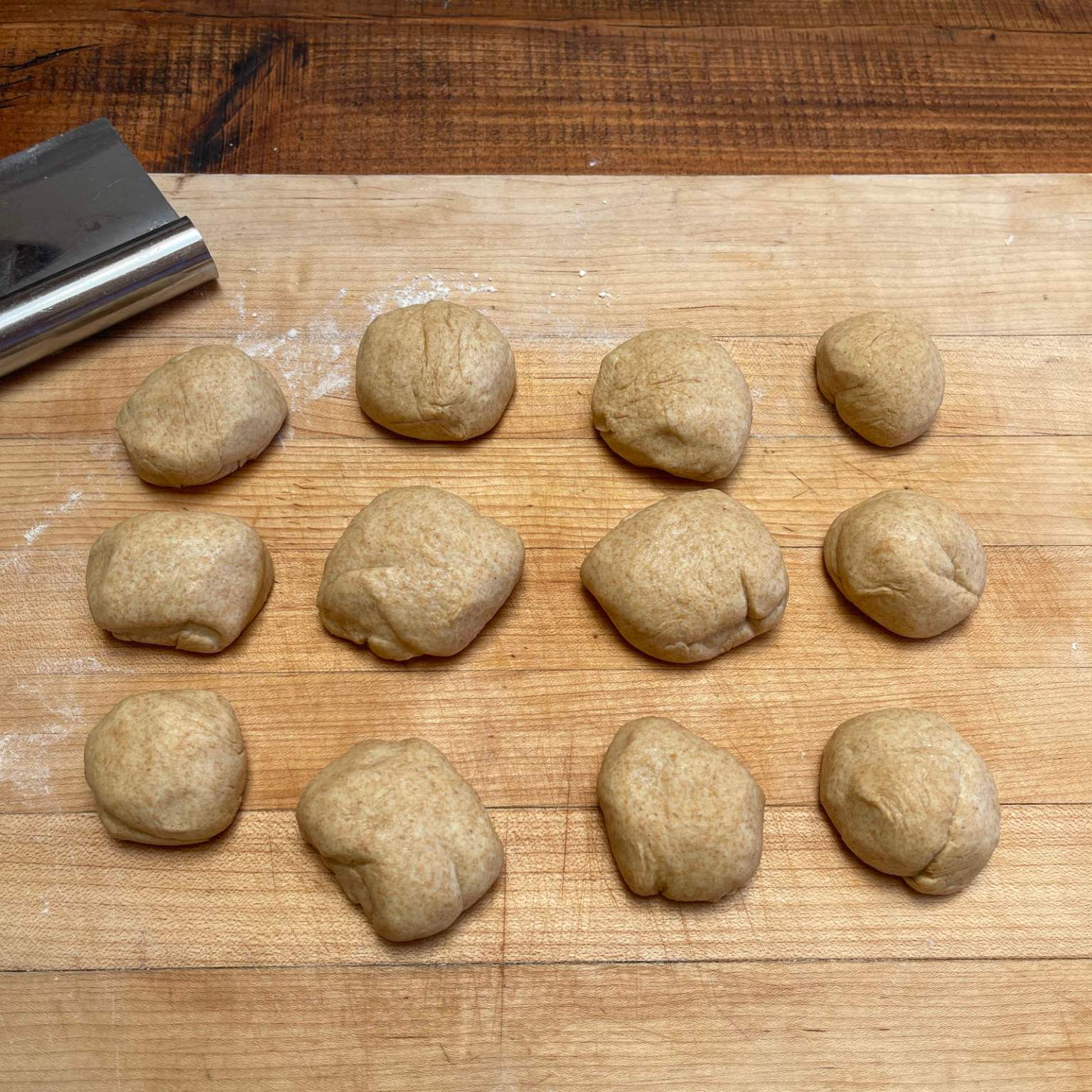 12 balls of wheat tortilla dough sit on a wooden board