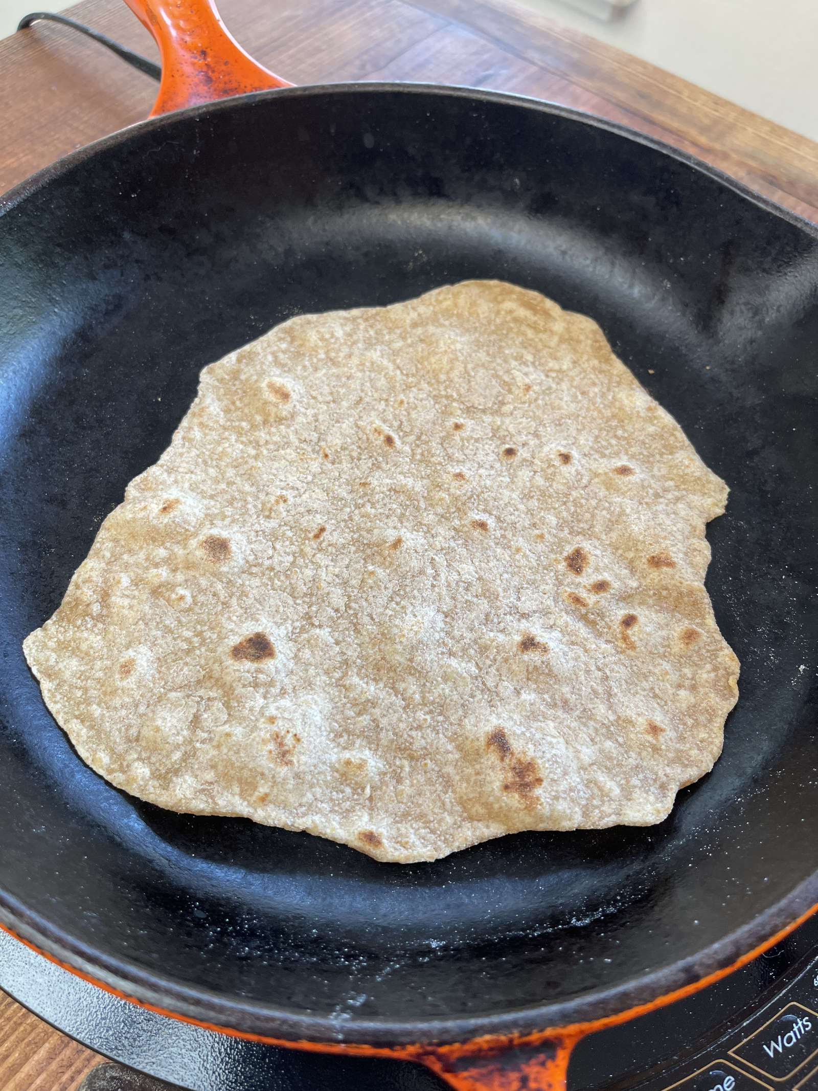 A flipped wheat tortilla cooking in an enameled cast iron pan