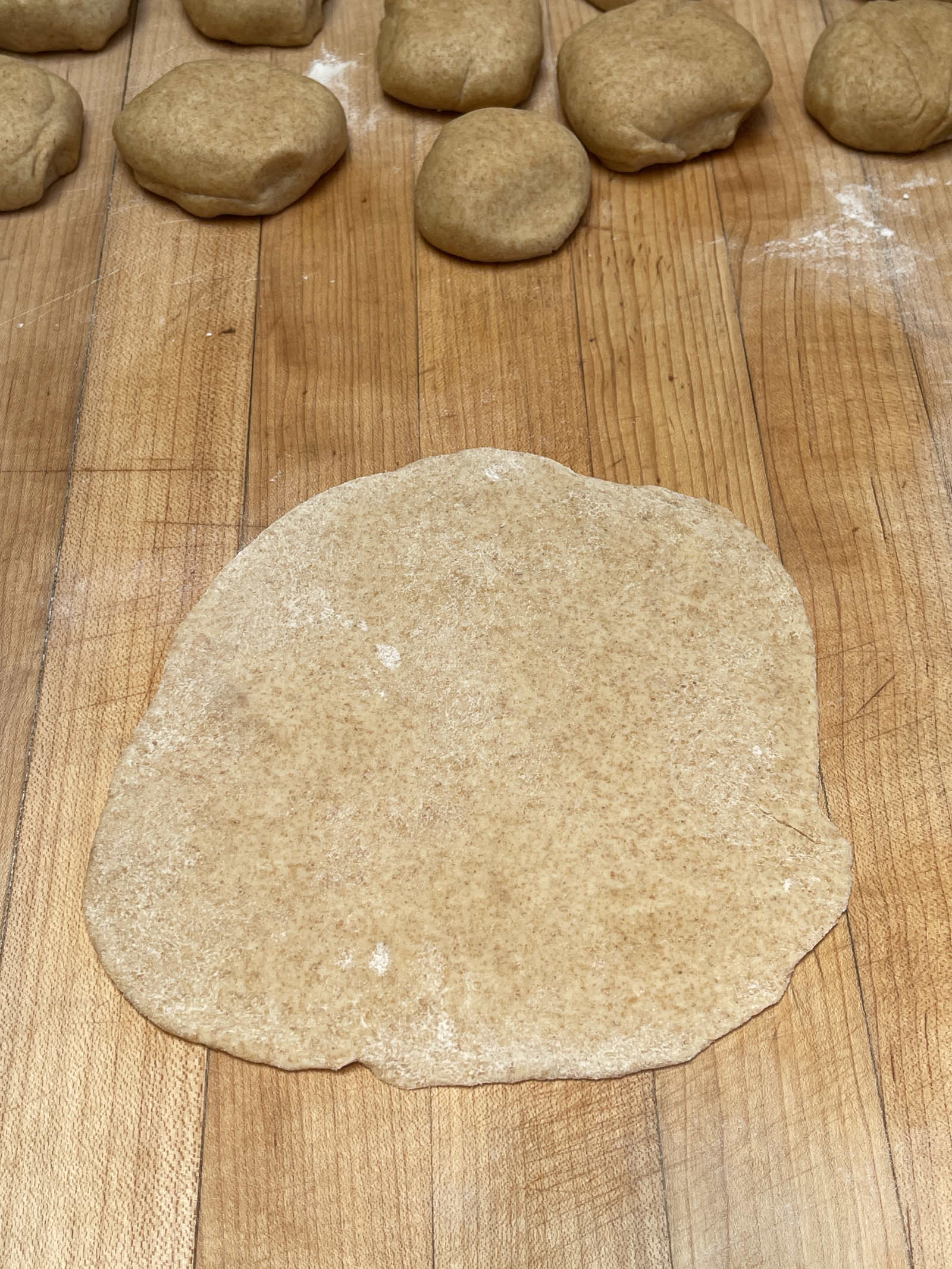 A rolled out tortilla sits on a wooden cutting board