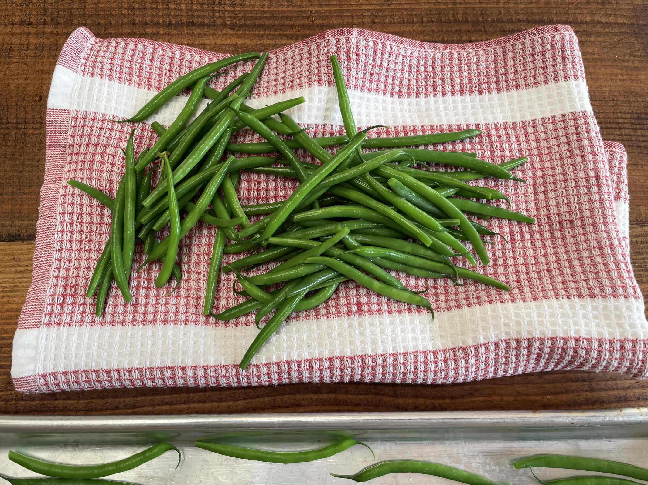 Blanched green beans drain on a red checked cotton dishtowel sitting on a dark wooden table