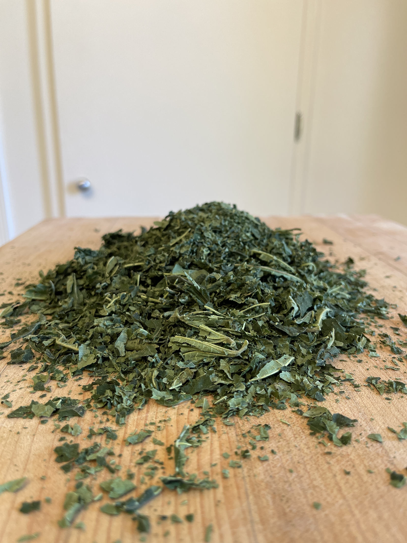 A large pile of fig leaf tea sits on a blond wooden cutting board