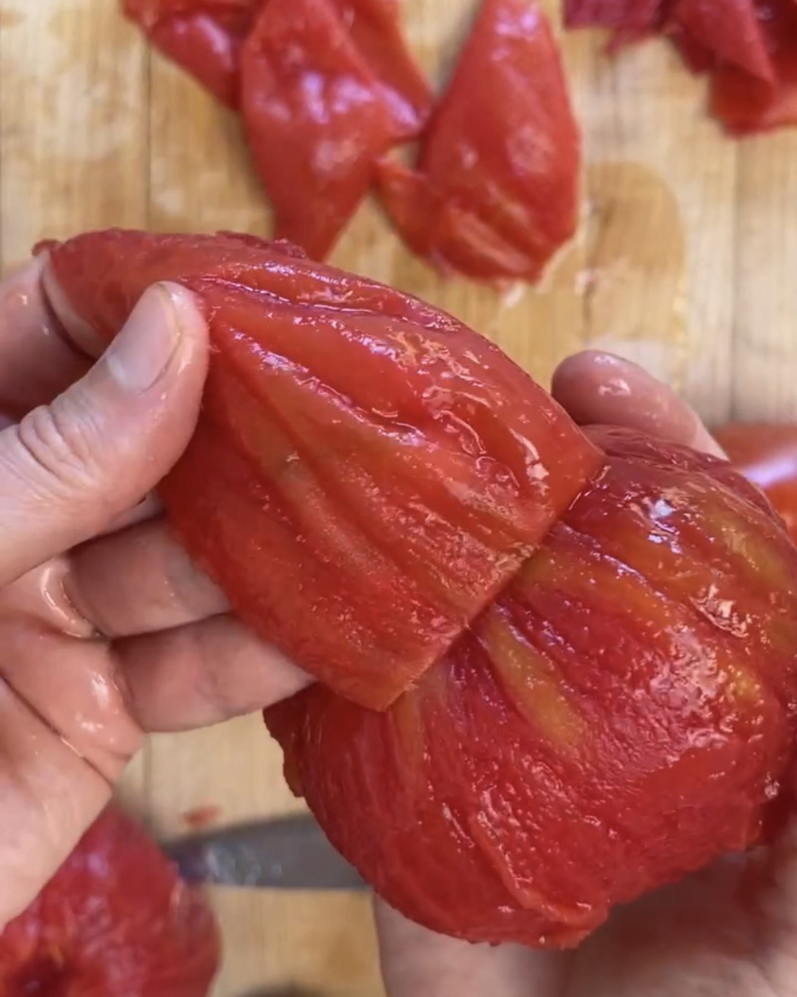 A hand pulls the skin off of a blanched tomato