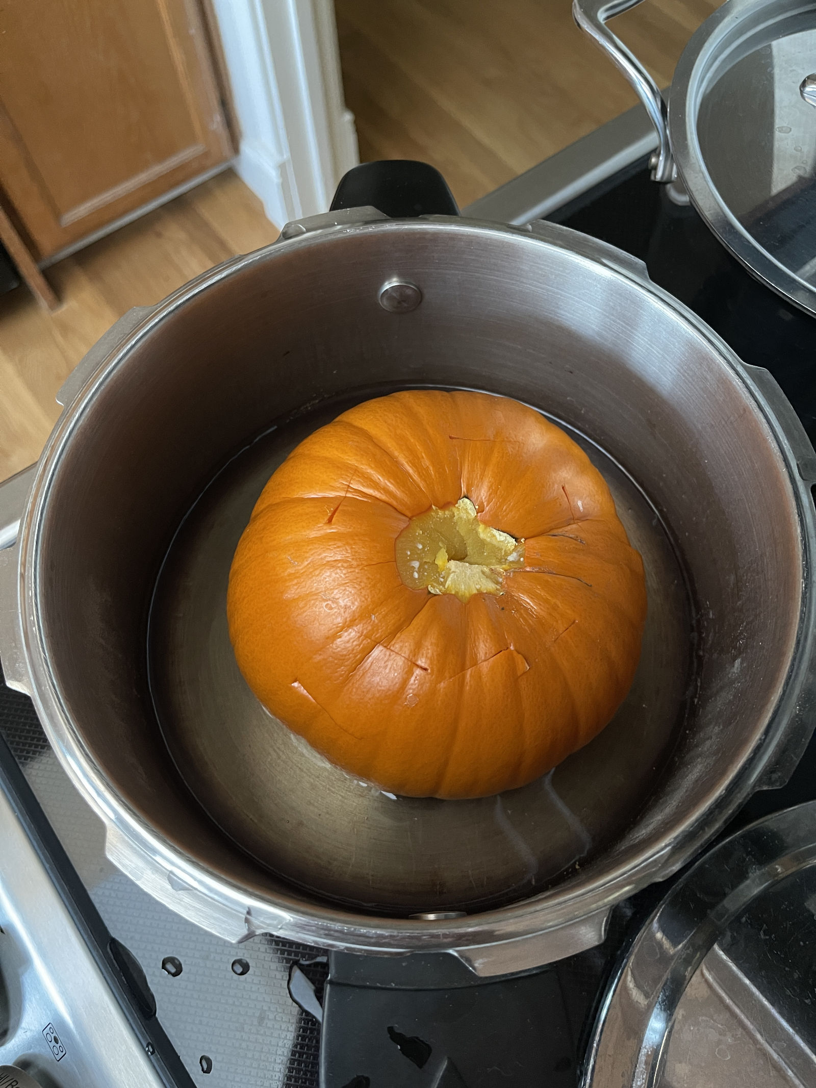 A cooked sugar pie pumpkin and a small amount of water sit inside a pressure cooker sitting on top of a range