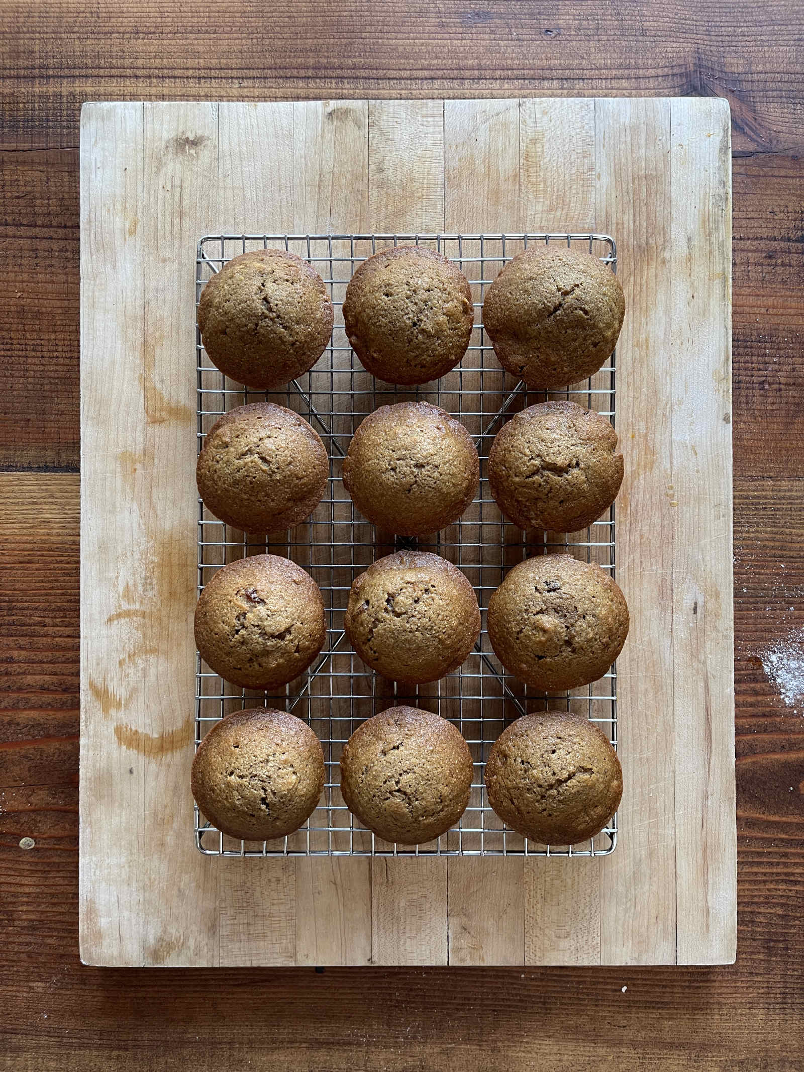 12 pumpkin spice muffins cool on a wire rack set on a light wooden cutting board sitting on a dark wood table