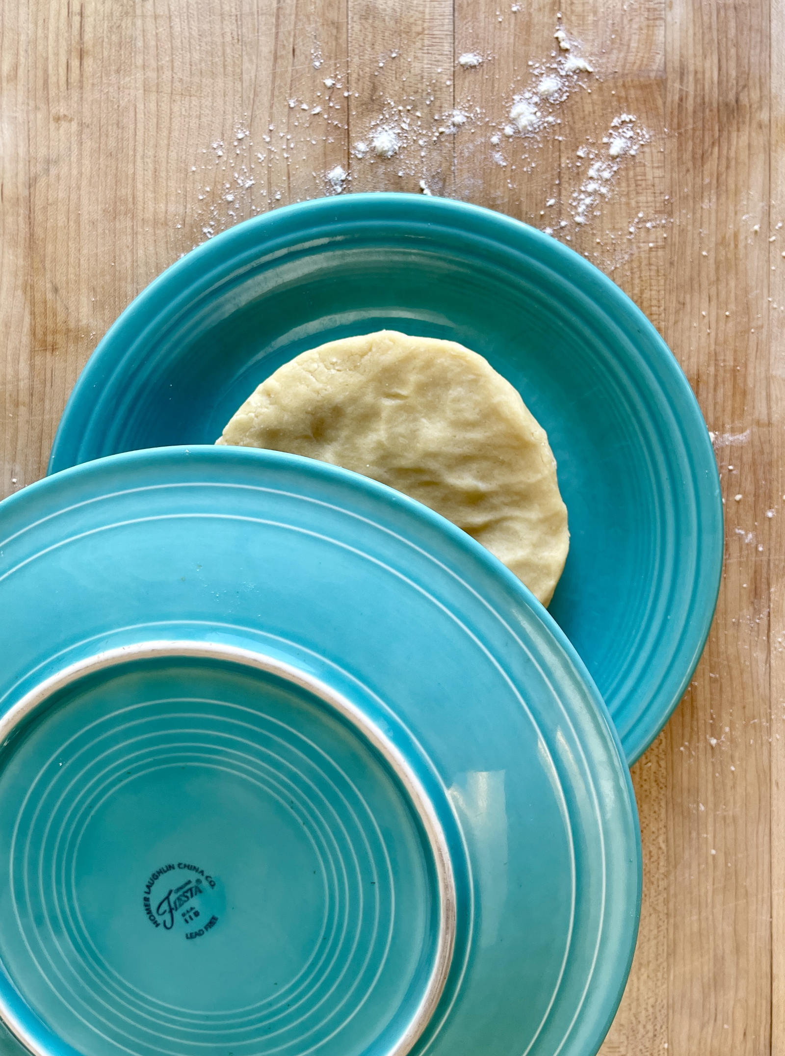 An inverted turquoise Fiesta Ware plate is about to cover another turquoise plate holding a disk of semolina pastry