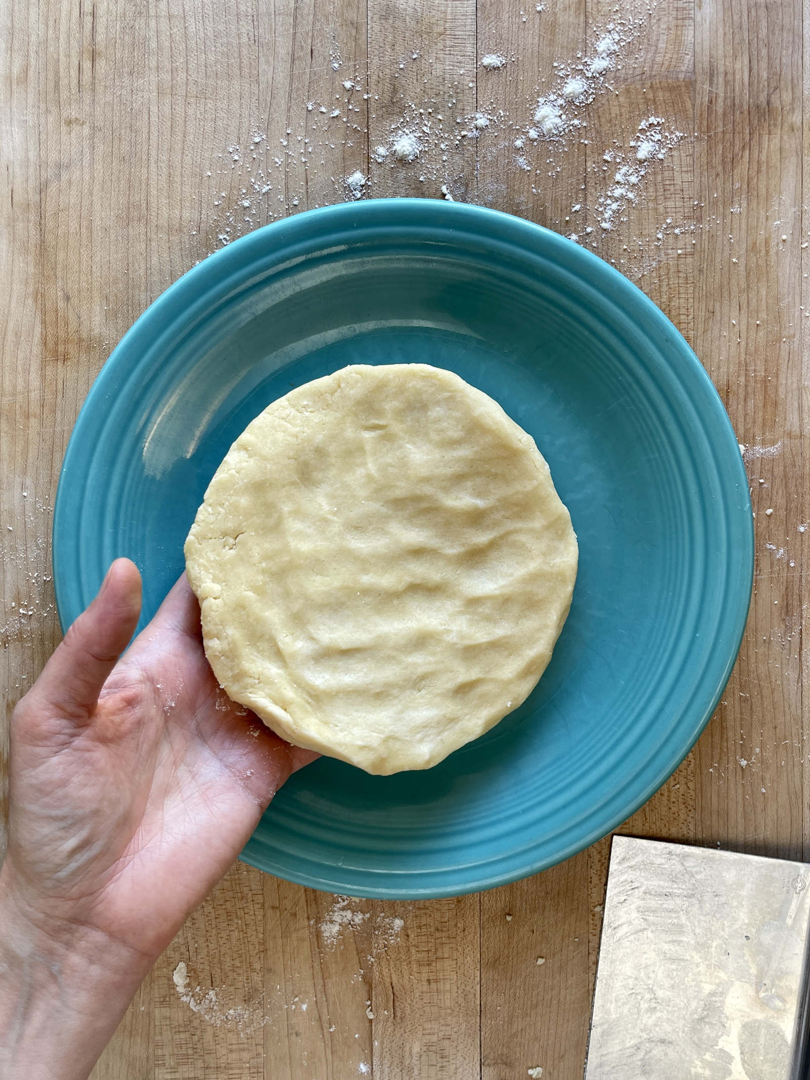 A hand places a disk of semolina pastry on a turquoise colored plate